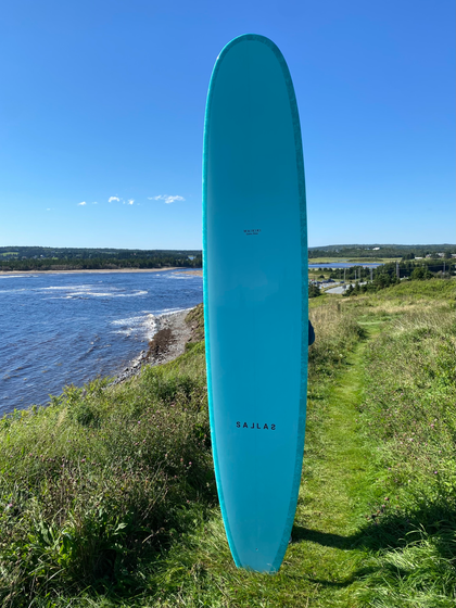 Kai Sallas blue longboard surfboard on the MacDonald House bluff in Lawrecetown, Nova Scotia.